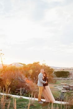 Groom hugging bride standing on stone path at sunset. High quality photo