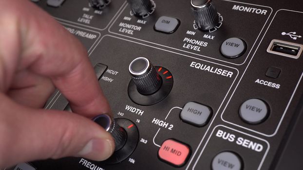 A sound engineer adjusts frequencies on a digital audio mixer. The man presses the buttons and turns the toggle switches on the sound console. Close-up of a man's hand. 4k