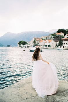 Bride holds the hem of her dress in her hand on the banks of Perast. High quality photo