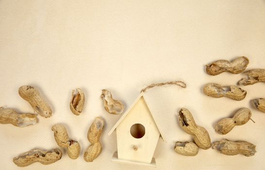 Beautiful birdhouse on beige background with peeled peanuts, top view. Space for text, spring bird food concept copy space