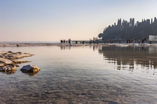 A stunning landscape photo of a rocky beach in Sirmione, with the clear waters of Lake Garda in the background