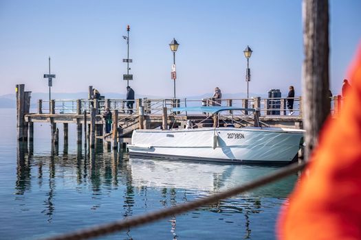 Sirmione, Italy 15 February 2023: A peaceful and picturesque view of Sirmione's marina with colorful boats docked at the pier, set against a beautiful natural landscape.