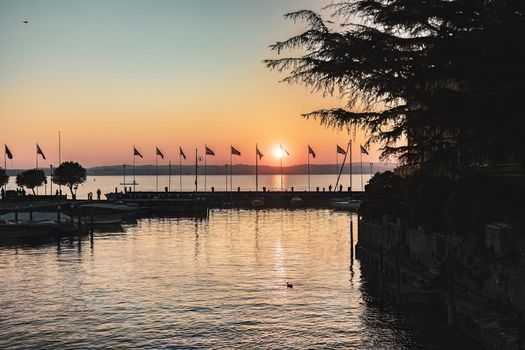 Sirmione, Italy 15 February 2023: Beautiful sunset over the stunning Garda Lake in Italy, with the sun reflecting on the calm water and creating a peaceful atmosphere. Perfect for travel projects.