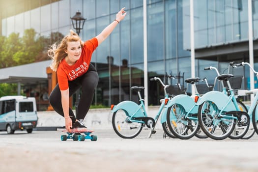 Young blonde caucasian girl having fun outside on a skateboard, wearing black leggings and red shirt, sun flare. Teen girl laughing, having fun outside in the summer.