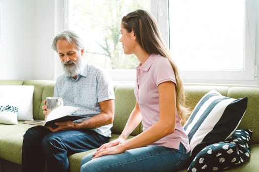 Young caucasian woman taking care of her grandfather, senior man with beard and grey hair. Granddaughter visiting her grandfather, spending quality time together.