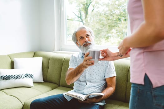 Young caucasian woman taking care of her grandfather, senior man with beard and grey hair. Granddaughter visiting her grandfather, spending quality time together.