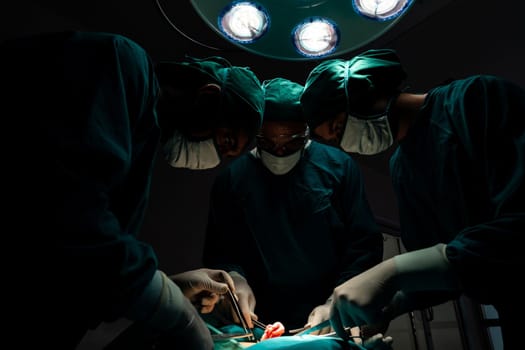 Surgical team performing surgery to patient in sterile operating room. In a surgery room lit by a lamp, a professional and confident surgical team provides medical care to an unconscious patient.