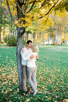 Man hugs woman standing under a plane tree with yellow leaves. High quality photo