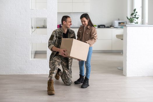 Happy military serviceman holding cardboard box with girl.