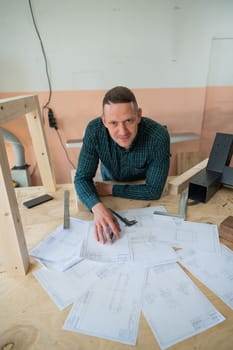 Portrait of a carpenter in a plaid shirt draws a workshop blueprint