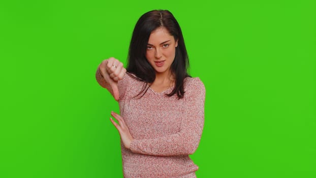 Dislike. Upset unhappy pretty woman in sweater showing thumbs down sign gesture, expressing discontent, disapproval, dissatisfied dislike. Young adult girl. Indoor studio shot on chroma key background