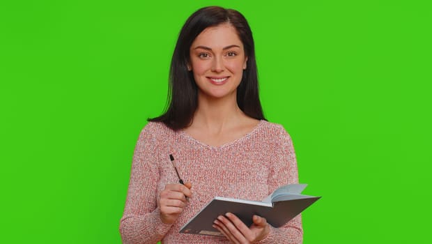 Thoughtful journalist pretty young woman in sweater making notes, writing down thoughts with pen into notepad notebook diary, to do list, good idea. Millennial girl isolated on chroma key background