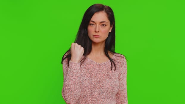 Angry aggressive woman trying to fight at camera, shaking fist, boxing with expression, punishment, disappointment, rage, quarrel. Young adult girl isolated alone on green screen chroma key background