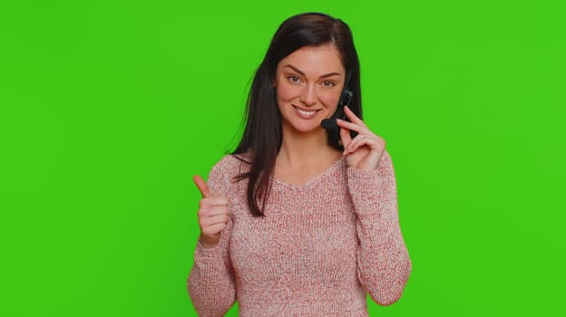 Smiling woman wearing headset, freelance worker, call center or support service operator helpline, having talk with client or colleague communication support. Young girl on green chroma key background