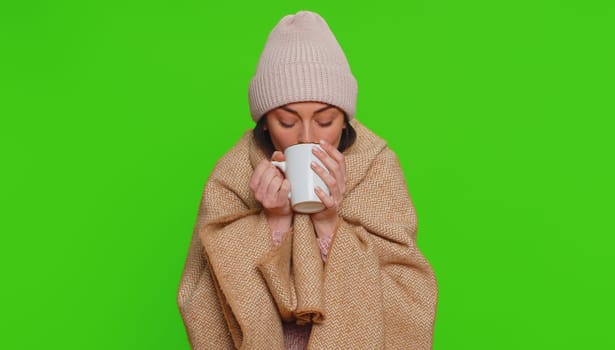 Sick woman wear hat wrapped in plaid shivering from cold, drinking hot tea in unheated apartment without heating due debt. Unhealthy girl feeling discomfort try to warming up on chroma key background