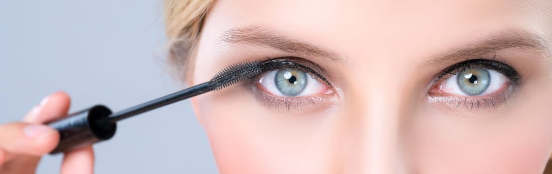 Closeup woman with blond hair putting alluring black mascara with brush in hand on long thick eyelash. Perfect fashionable cosmetic clean facial skin with beautiful eye young woman in high resolution.