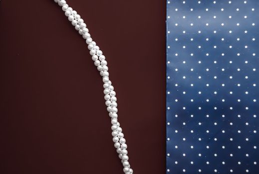 Pearl jewellery necklace and abstract blue polka dot background on chocolate backdrop.