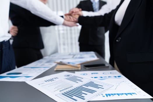 Focus financial report with statistic charts analyzed by BI papers on meeting table at conference room with blur business colleague people put hand stack together in background as harmony concept.