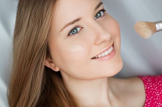 Beautiful woman applying liquid make-up foundation on her skin with make-up brush.