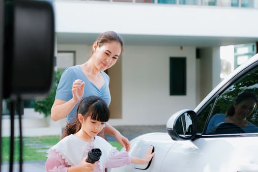 Progressive lifestyle of mother and daughter who have just returned from school in an electric vehicle that is being charged at home. Electric vehicle powered by sustainable clean energy.