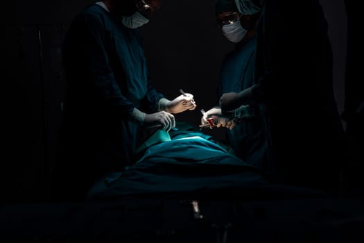 Surgical team performing surgery to patient in sterile operating room. In a surgery room lit by a lamp, a professional and confident surgical team provides medical care to an unconscious patient.