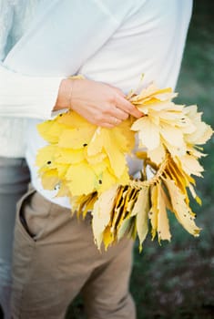 Wreath of yellow leaves in woman hand embracing man. Close-up. High quality photo