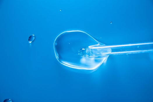 Water bubbles with cosmetic liquid drops of serum on a blue background of a laboratory glass pipette. Close-up of a pipette with drops.