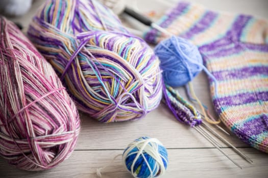 Colored threads, knitting needles and other items for hand knitting, on a light wooden table .