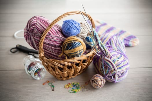 Colored threads, knitting needles and other items for hand knitting, on a light wooden table .