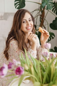 A brown-haired woman with long hair is having breakfast at the table with croissants and a cup of coffee. Spring portrait