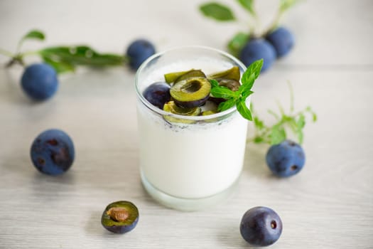 sweet homemade yogurt with fresh plum slices in a glass on a wooden table