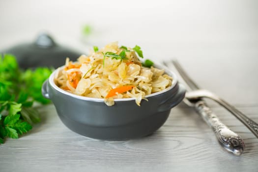 Braised cabbage with carrots, onions and herbs in a ceramic bowl on a wooden table.