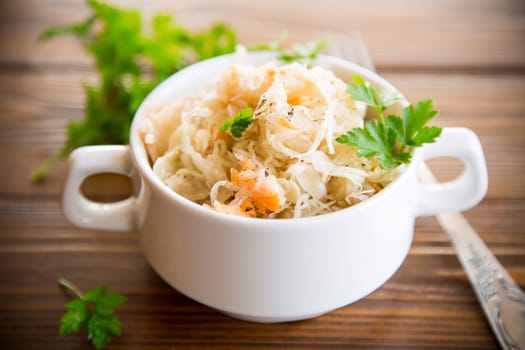 sauerkraut with carrots and spices in a bowl on a wooden table.