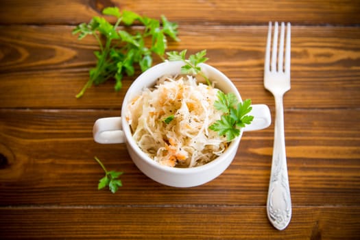 sauerkraut with carrots and spices in a bowl on a wooden table.