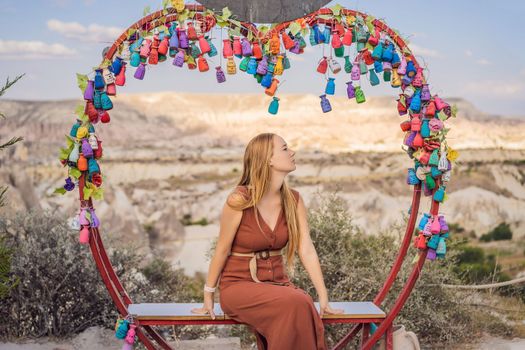 Young woman exploring valley with rock formations and fairy caves near Goreme in Cappadocia Turkey. Wish tree. Small multi-colored jugs with inscriptions, wishes hanging on the branches of a tree., against the backdrop of sand ruins and blue sky.