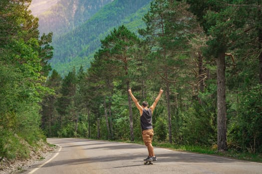 Hipster guy with long board with open arms enjoying life in the middle of a mountain road and a beautiful landscape. High quality photo