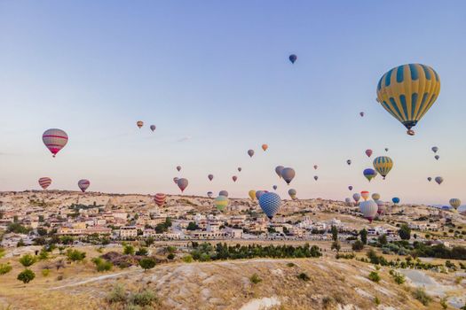 Colorful hot air balloons flying over at fairy chimneys valley in Nevsehir, Goreme, Cappadocia Turkey. Spectacular panoramic drone view of the underground city and ballooning tourism. High quality.