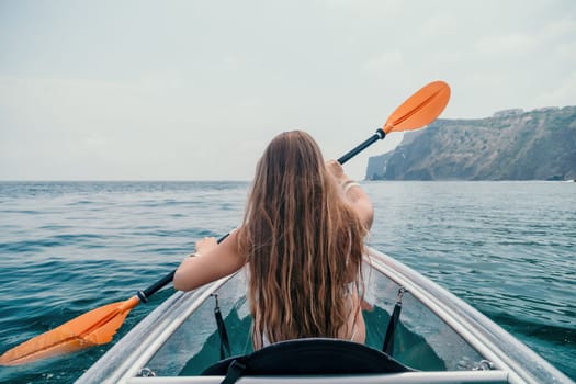 Woman in kayak back view. Happy young woman with long hair floating in transparent kayak on the crystal clear sea. Summer holiday vacation and cheerful female people having fun on the boat.