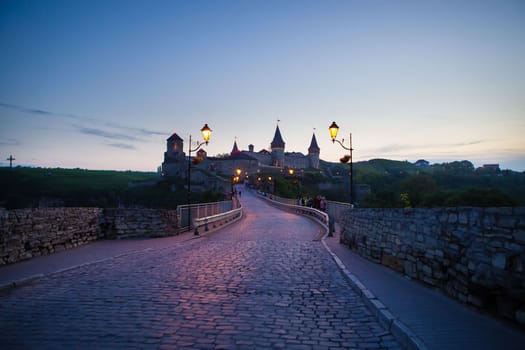 Kamianets-Podilskyi is a romantic city, a beautiful view of the evening city, lanterns illuminate the bridge. A picturesque summer view of the ancient castle-fortress in Kamianets-Podilskyi, Khmelnytskyi region, Ukraine