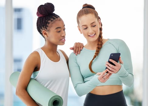 Look at this new yoga app. two young women standing together and using a cellphone after their yoga practise in the studio