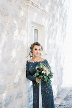 Bride in a blue lace dress leaned against the wall of a stone house. High quality photo