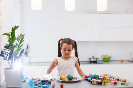 Little girl painting Easter eggs in the kitchen