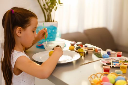 Little girl painting Easter eggs in the kitchen