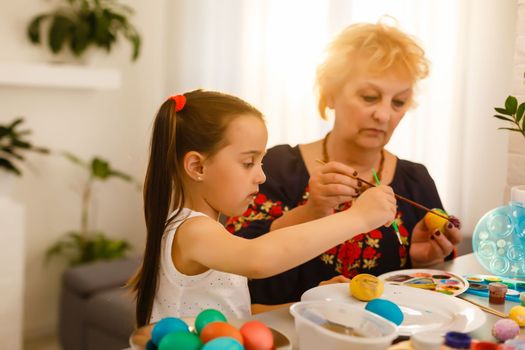 Grandmother with granddaughter are coloring eggs for Easter.