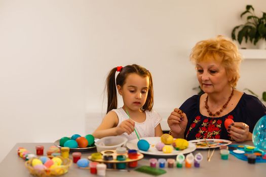 Grandmother with granddaughter are coloring eggs for Easter.