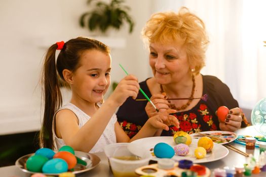 Grandmother with granddaughter are coloring eggs for Easter.