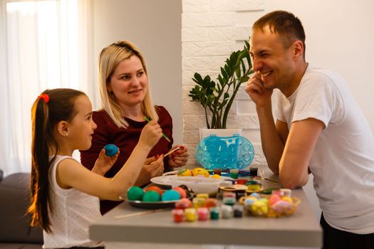 Little child with parents painting Easter eggs at home.