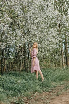 Blonde girl on a spring walk in the garden with cherry blossoms. Female portrait, close-up. A girl in a pink polka dot dress