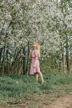 Blonde girl on a spring walk in the garden with cherry blossoms. Female portrait, close-up. A girl in a pink polka dot dress