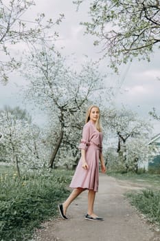 Blonde girl on a spring walk in the garden with cherry blossoms. Female portrait, close-up. A girl in a pink polka dot dress